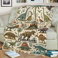 Close view of dinosaur throw blanket on a sofa featuring detailed prehistoric animals, palms, flowers, and ocean waves