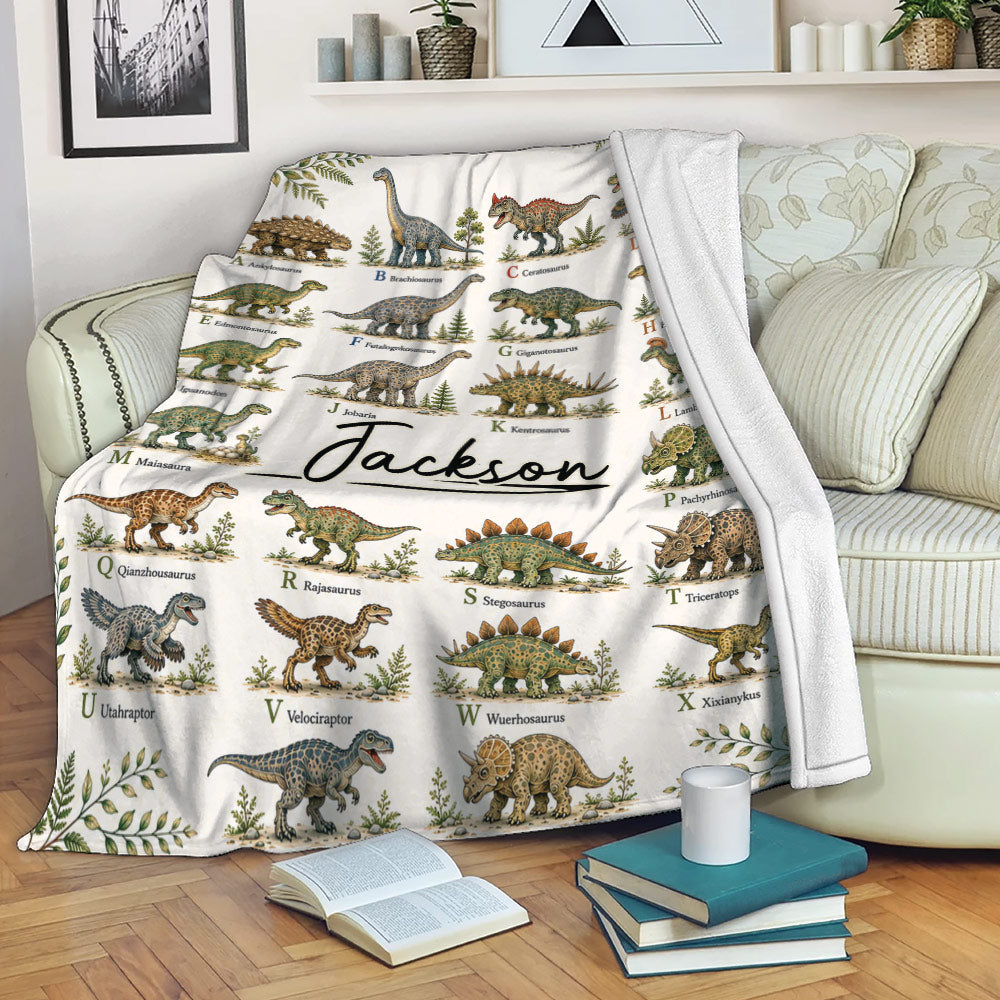 Dinosaur alphabet blanket draped over a sofa with illustrated prehistoric creatures and leafy accents