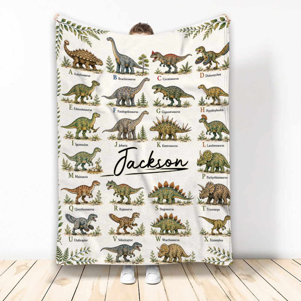 Dinosaur alphabet throw blanket featuring illustrated prehistoric creatures and botanical border artwork