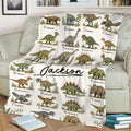 Dinosaur throw blanket displayed on a sofa with colorful prehistoric creature illustrations and alphabet labels