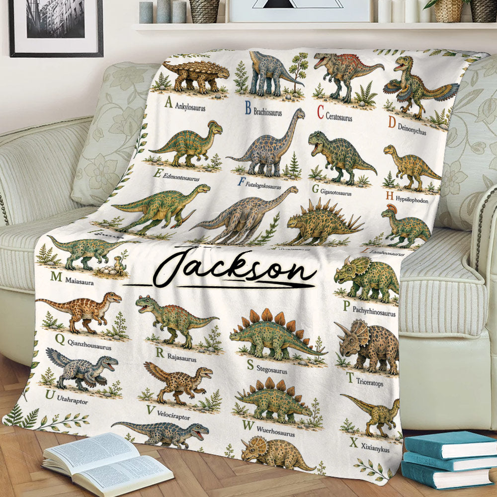 Dinosaur throw blanket displayed on a sofa with colorful prehistoric creature illustrations and alphabet labels