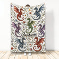 Dragon throw blanket displayed upright with colorful red, blue, green, and purple dragons on a floral fantasy pattern