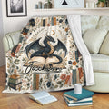 Dragon throw blanket draped over a sofa with moon, books, flowers, and dark fantasy artwork