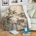 Duck hunting throw blanket displayed on a couch with mallards, reeds, and wetland artwork
