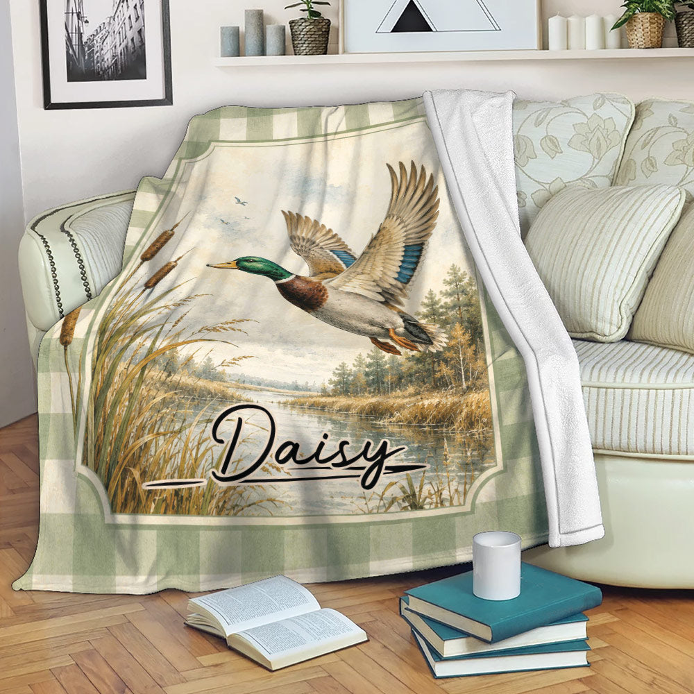 Duck hunting throw blanket displayed on a sofa with vintage mallard artwork and peaceful wetland scenery