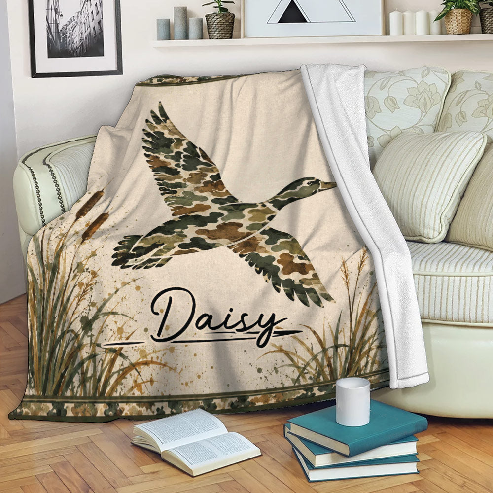 Duck hunting throw blanket displayed on a sofa with flying duck artwork, cattails, and camouflage details