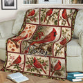 Red cardinal throw blanket spread across an armchair with floral, berry, pinecone, and winter bird scenes