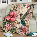 Colorful hummingbird throw blanket displayed on a sofa with hibiscus, lilies, and butterfly details