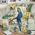 Colorful parrot blanket draped over a sofa, featuring tropical flowers, foliage, and blue bird artwork