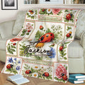 Close view of a ladybug throw blanket on a sofa featuring red ladybugs, flowers, and leafy garden details