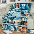 Surfing throw blanket displayed on a couch with surfers, tropical beach panels, waves, and coastal artwork