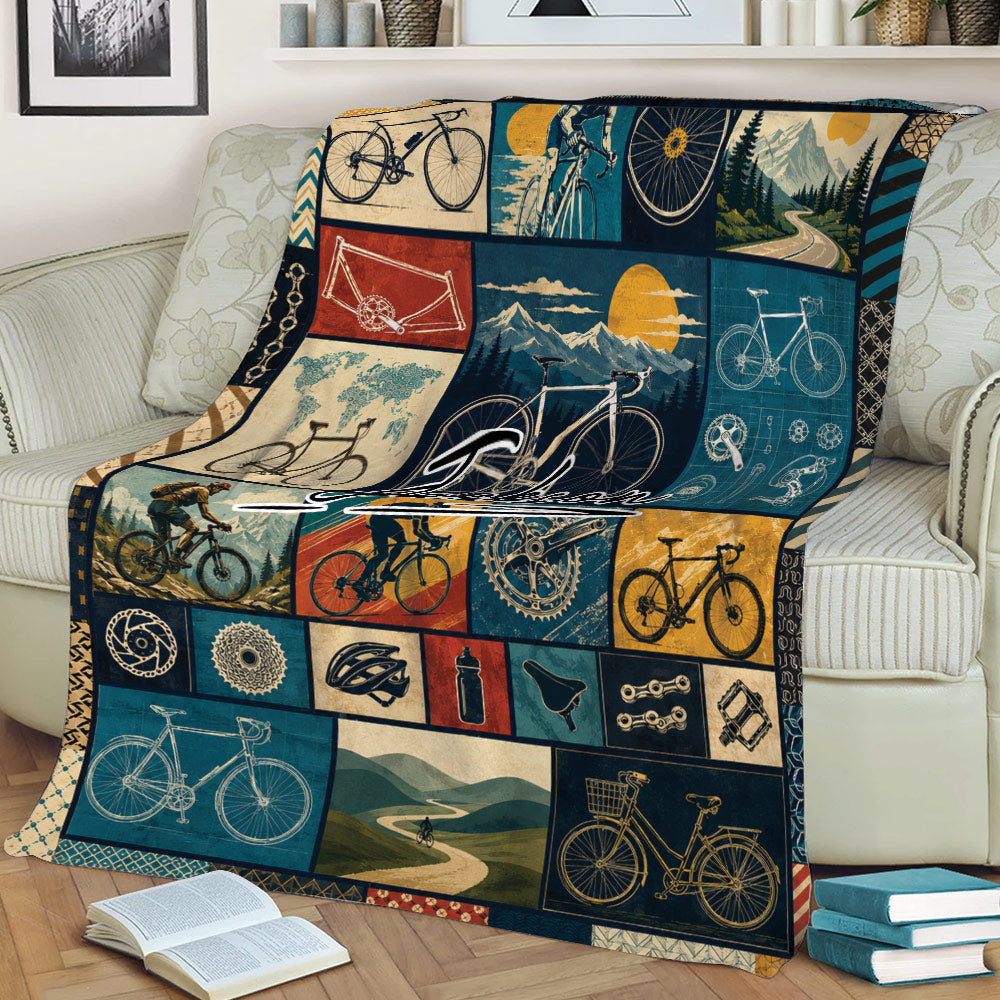 Cycling-themed throw blanket displayed on a couch with bicycle illustrations, mountain scenery, and bike parts