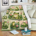 Frog throw blanket draped over a sofa with cheerful frog illustrations, lily pads, and floral pond artwork