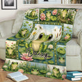 Frog throw blanket displayed on a couch with a large central frog surrounded by pond plants and flowers