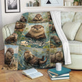 Otter throw blanket draped over a sofa, featuring illustrated river otters, ponds, flowers, and woodland colors