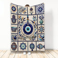 Evil Eye throw blanket with blue Nazar motifs, Hamsa symbols, botanical accents, and decorative pottery artwork