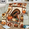 Thanksgiving throw blanket draped over a couch with turkey, pumpkins, pie, wreath, and fall artwork