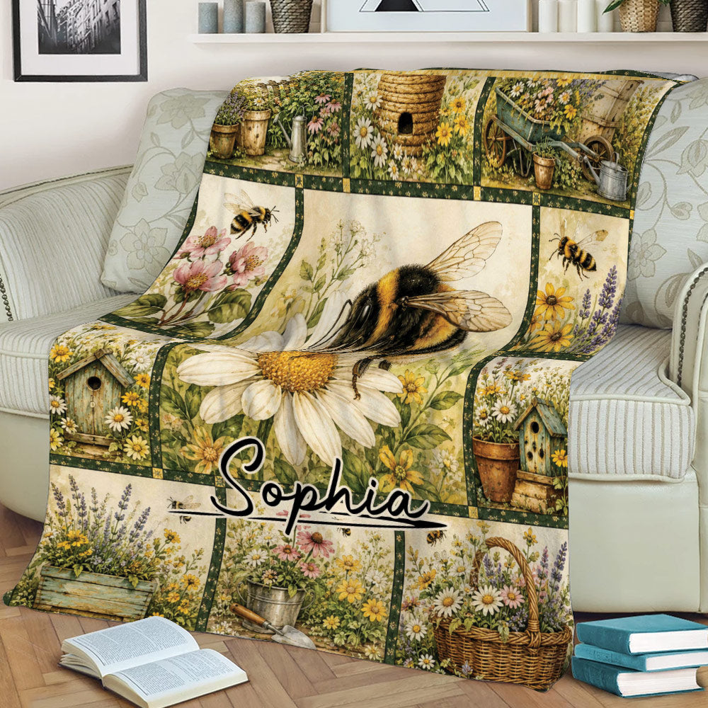 Bee blanket displayed on a sofa with a large bumblebee, daisies, lavender, flower baskets, and garden artwork