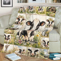 Rustic cow blanket displayed on a sofa with a large cow portrait, meadow flowers, barns, and countryside scenes