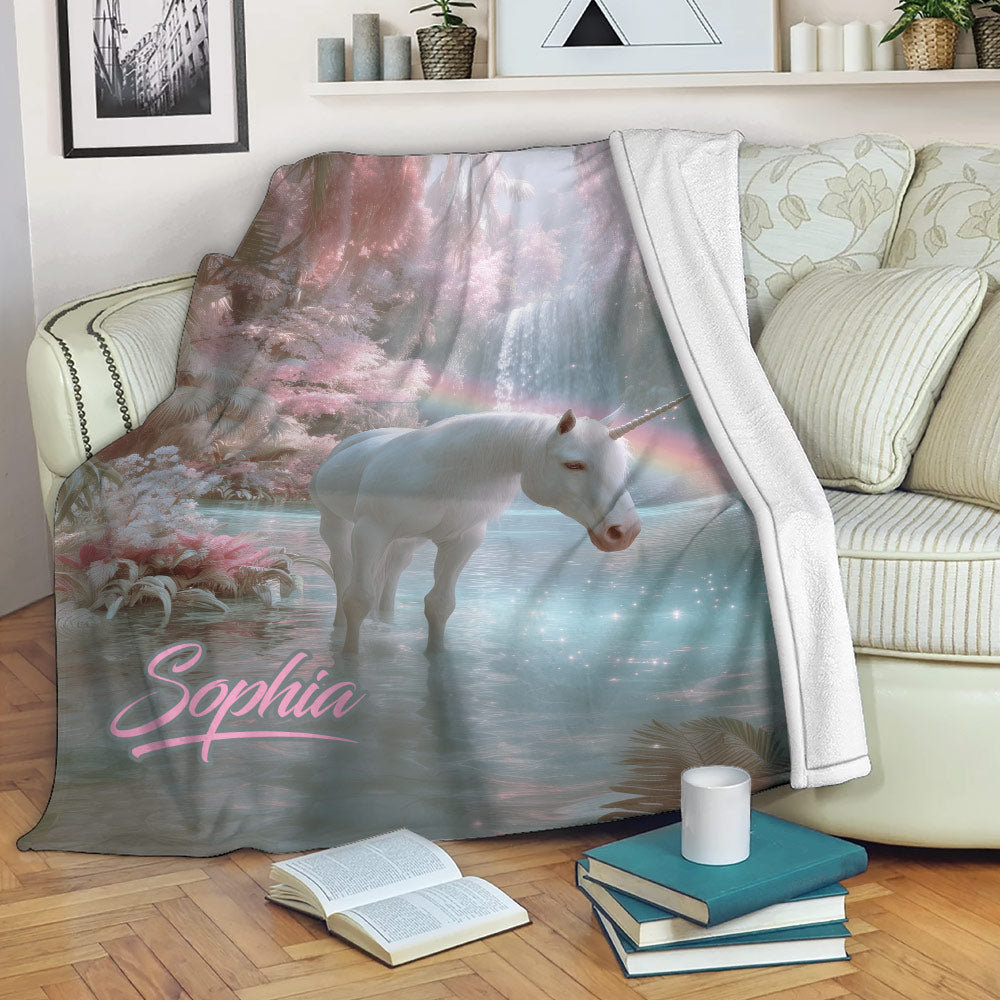 Pastel unicorn blanket draped over a sofa, showing a magical forest, waterfall, rainbow, and lake scene