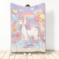Pastel unicorn throw blanket displayed upright with rainbows, balloons, flowers, stars, and heart details