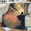 Sasquatch throw blanket styled on a sofa with detailed trees, foliage, and a sunset forest scene