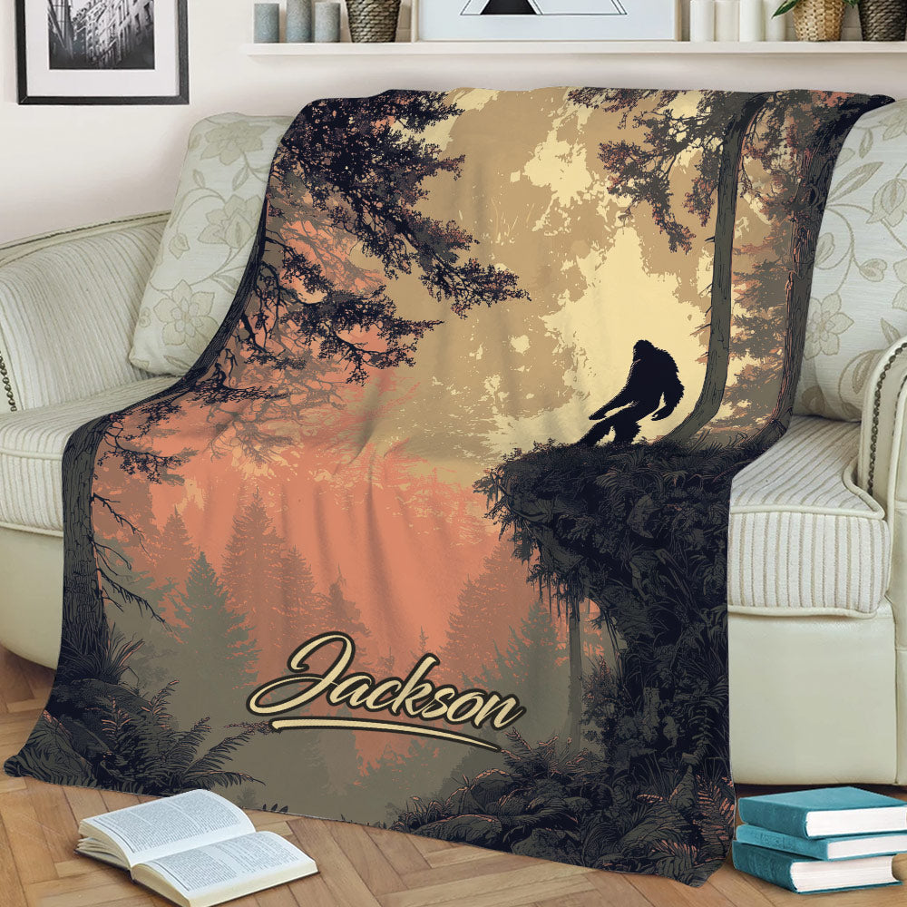 Sasquatch throw blanket styled on a sofa with detailed trees, foliage, and a sunset forest scene