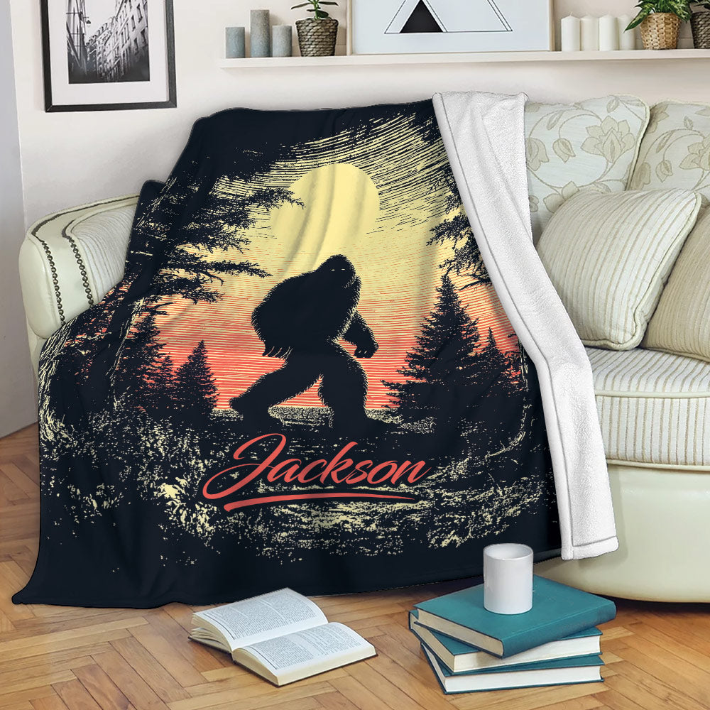 Custom Bigfoot blanket displayed on a sofa with a dramatic forest, moon, and sunset design