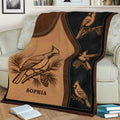 Cardinal blanket spread across a sofa featuring illustrated birds, pine branches, and warm rustic colors