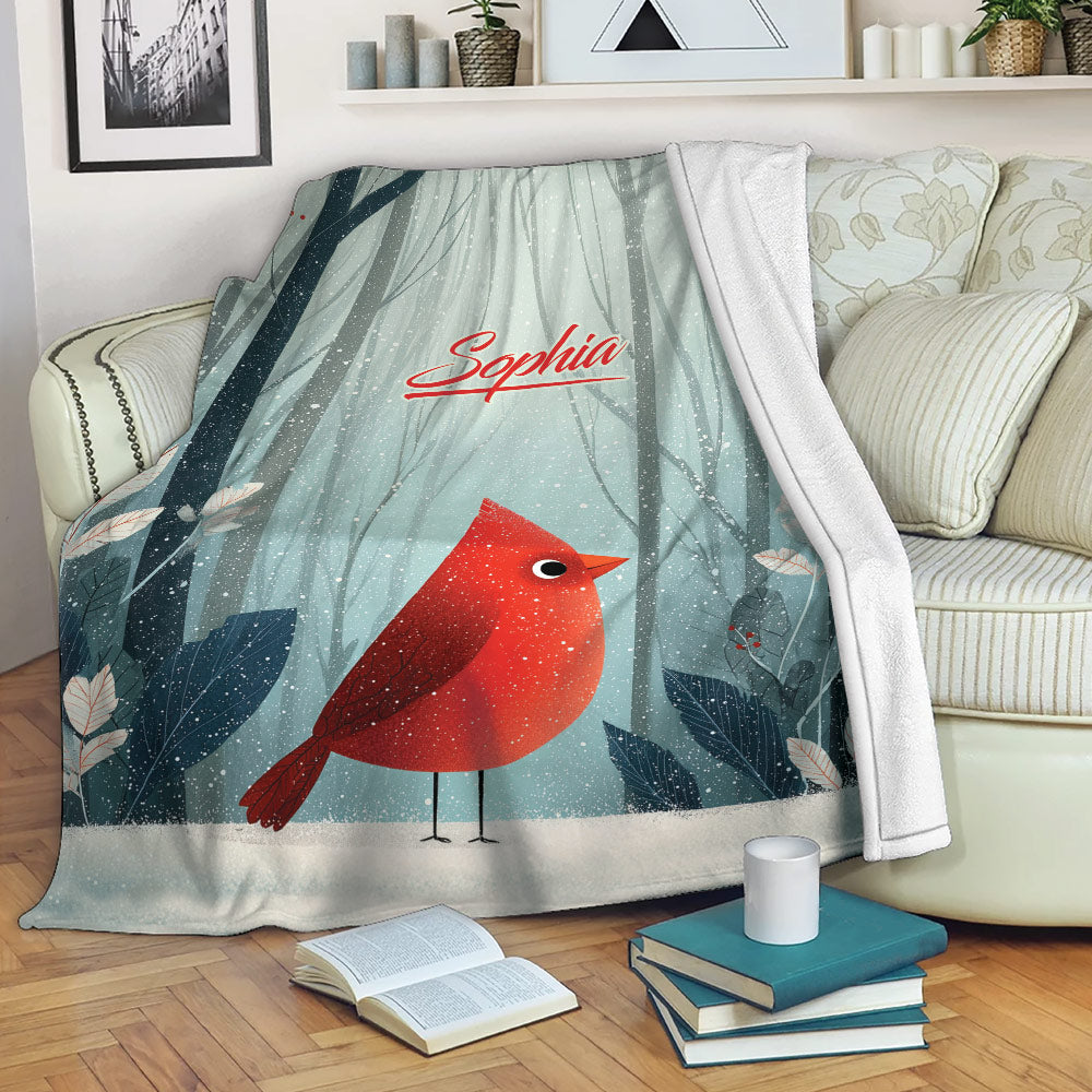 Cardinal blanket draped over a sofa, showing red bird artwork, winter forest scenery, and leafy details
