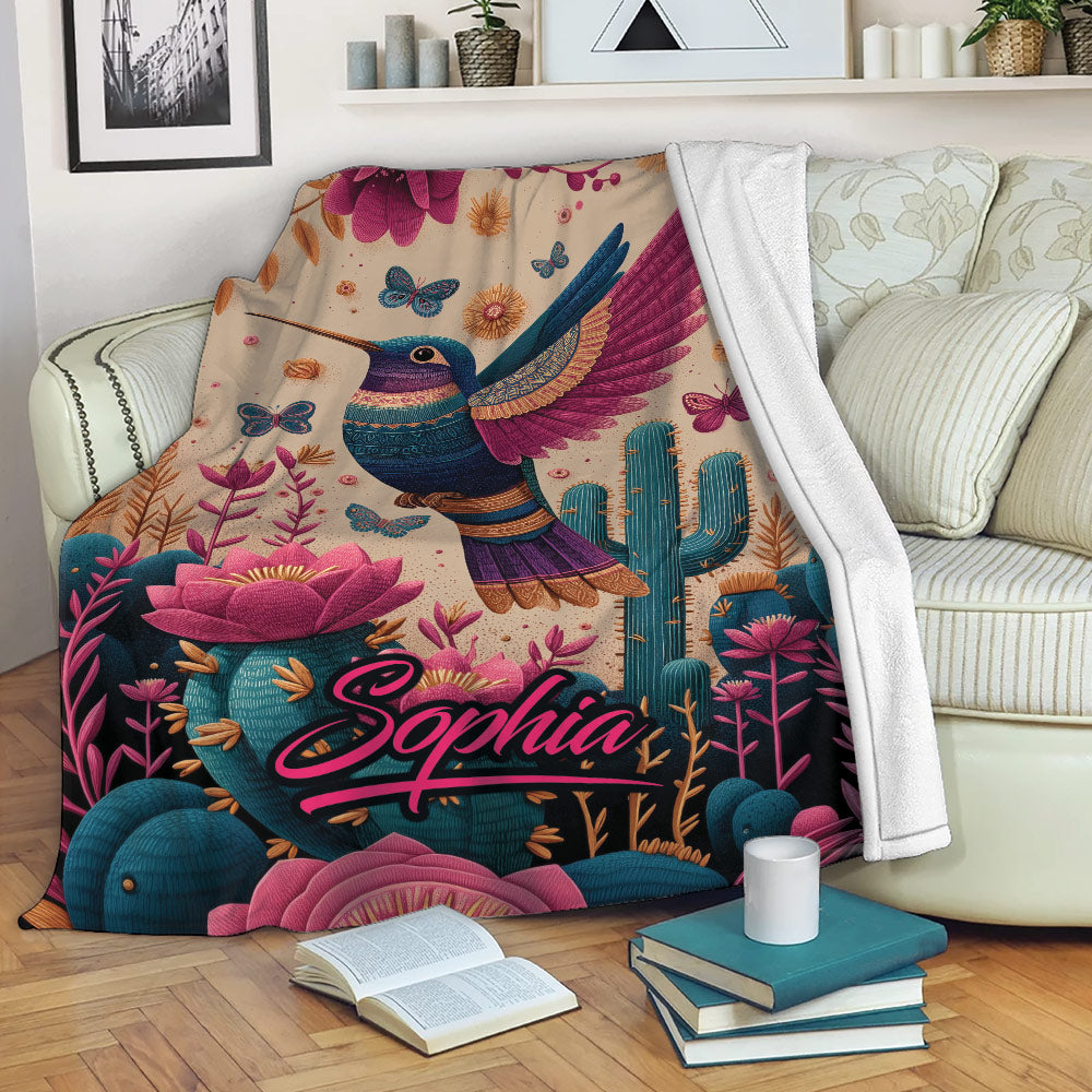 Hummingbird throw blanket draped over a sofa with vibrant flowers, butterflies, and desert plants
