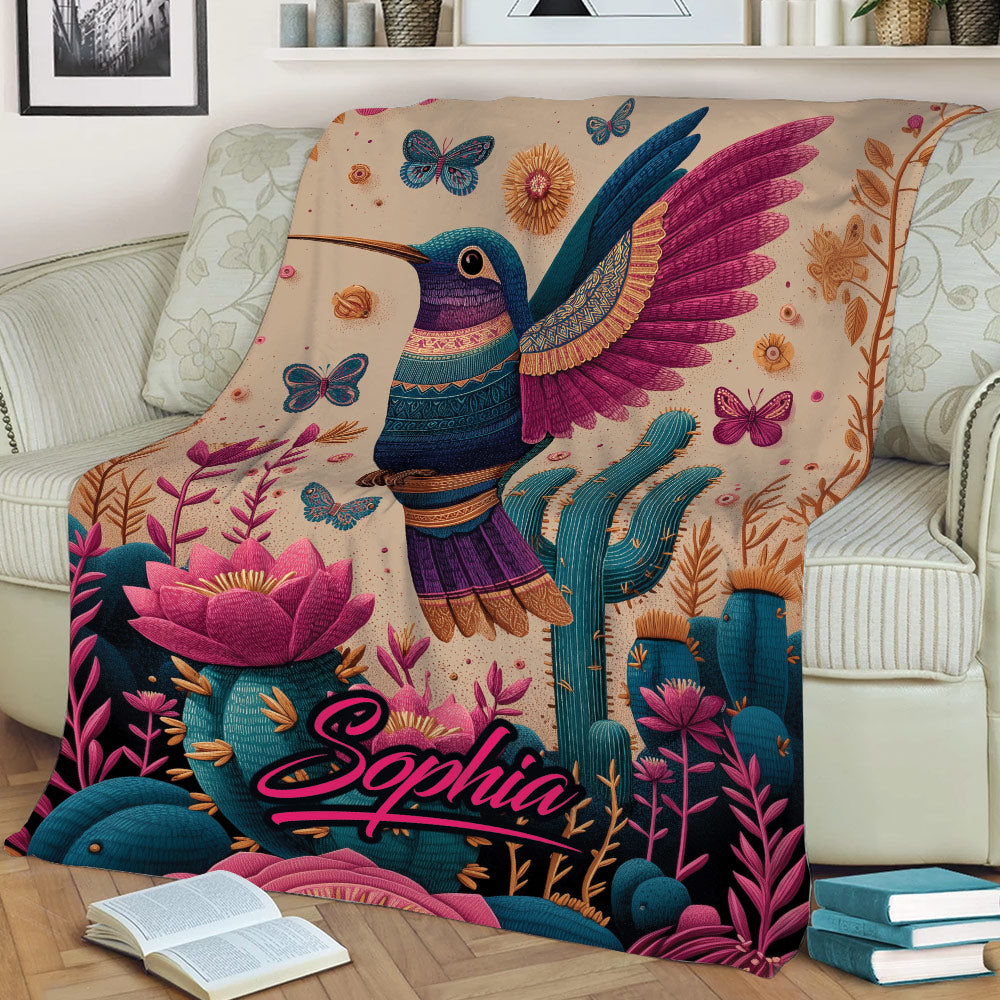 Detailed hummingbird blanket displayed on a sofa with colorful floral and cactus artwork