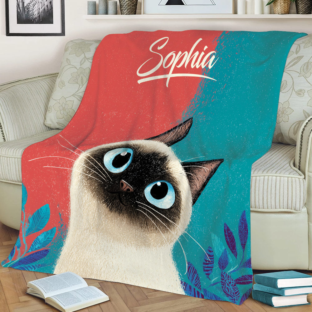 Siamese cat blanket displayed on a couch with expressive blue-eyed cat artwork and botanical accents