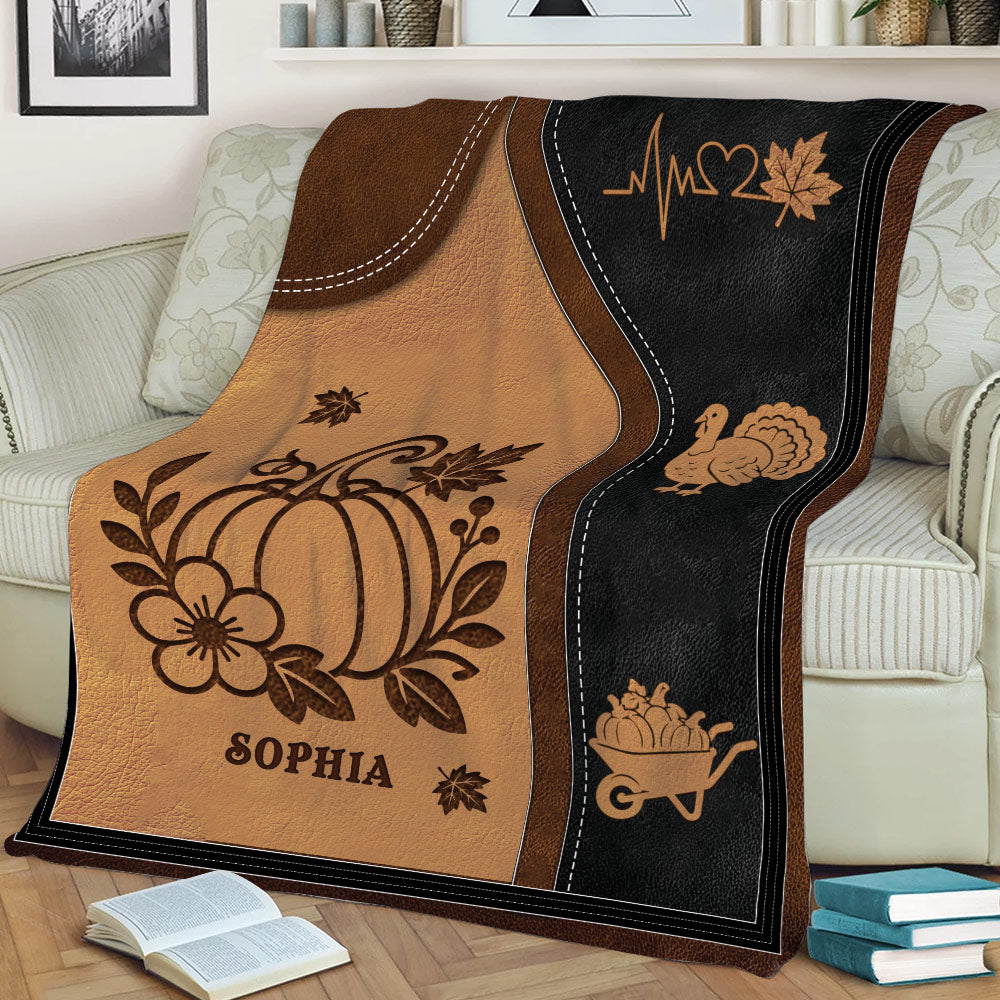 Harvest-themed autumn blanket displayed on a sofa with pumpkin, turkey, maple leaf, and wheelbarrow designs