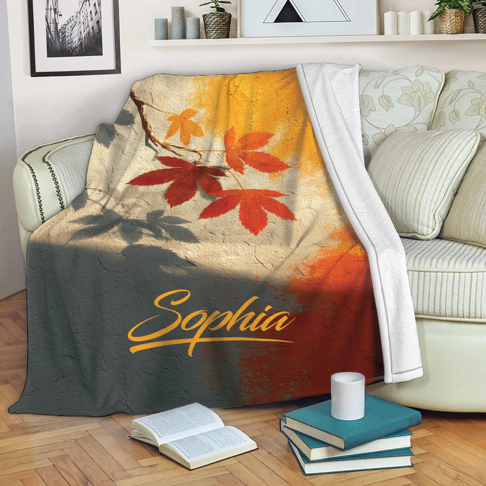 Autumn leaf blanket draped over a sofa in a cozy living room with books and a mug