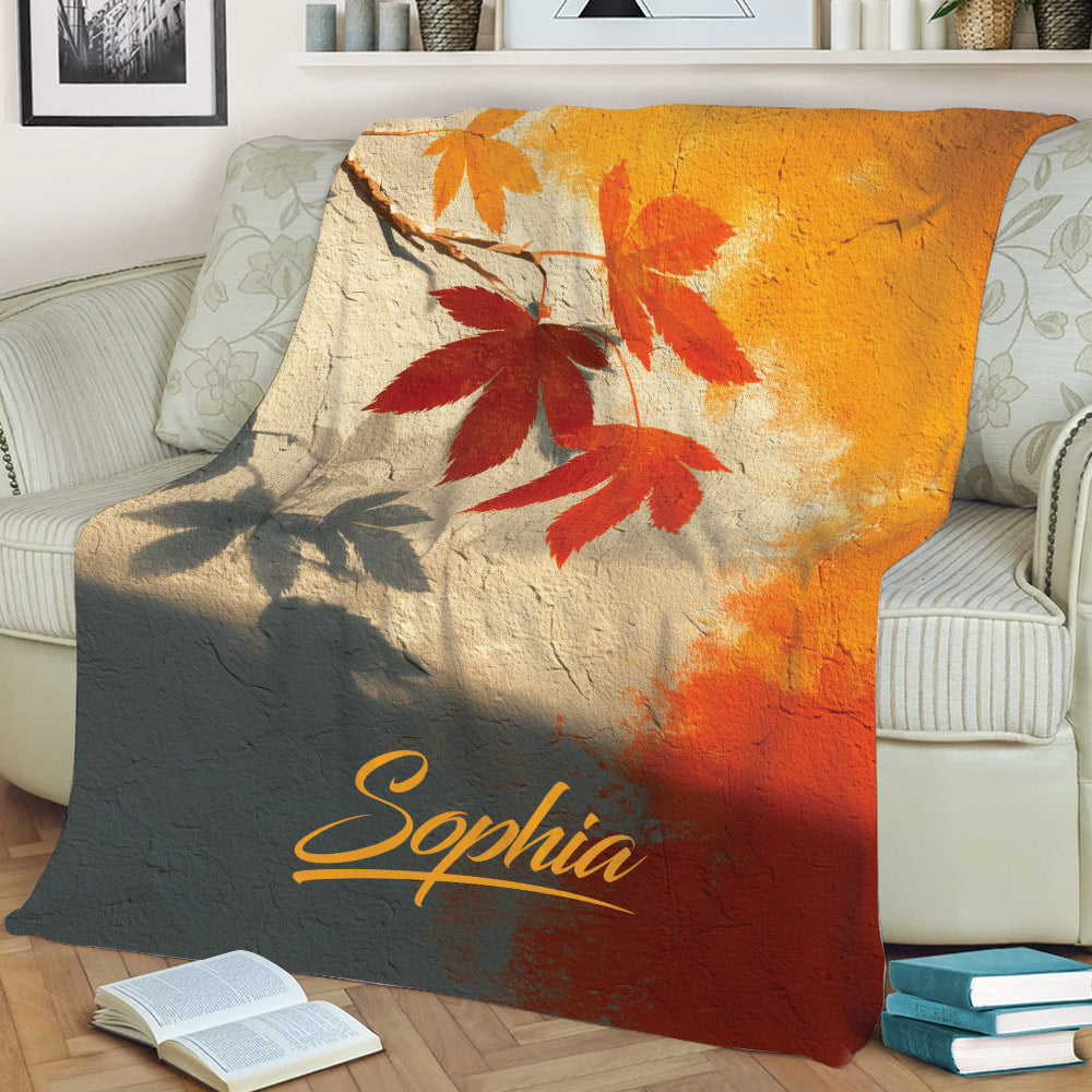 Warm-toned autumn leaf throw blanket arranged across a sofa with fall-inspired artwork