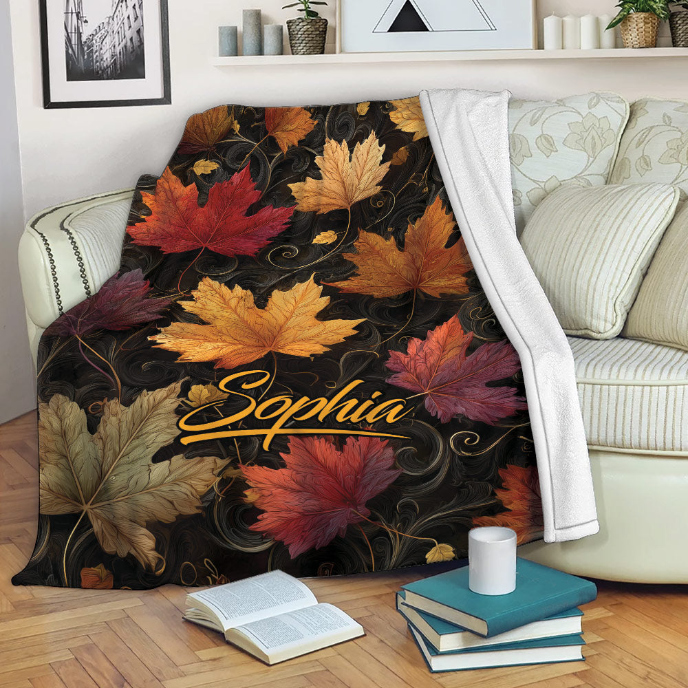 Autumn foliage throw blanket draped over a sofa with warm red, orange, gold, and burgundy leaves