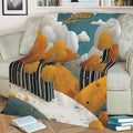 Fall landscape blanket displayed on a sofa with golden trees, wooded hills, clouds, and a warm seasonal palette