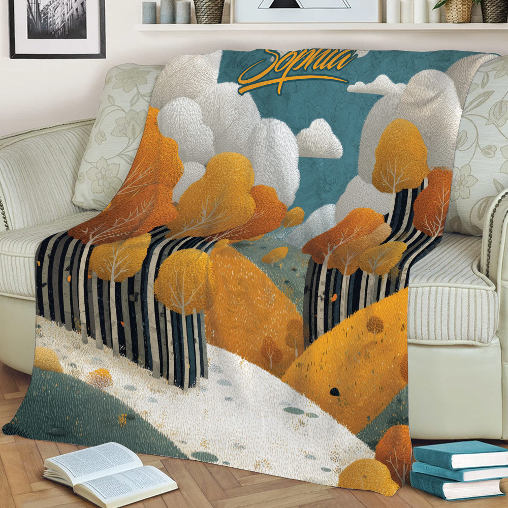 Fall landscape blanket displayed on a sofa with golden trees, wooded hills, clouds, and a warm seasonal palette