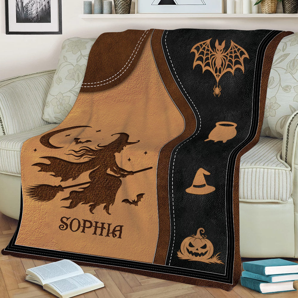 Halloween blanket displayed on a sofa with flying witch artwork, bats, spiderweb, witch hat, and pumpkin