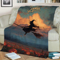 Halloween blanket displayed on a sofa with a broom-riding witch, pumpkins, and moody autumn landscape artwork