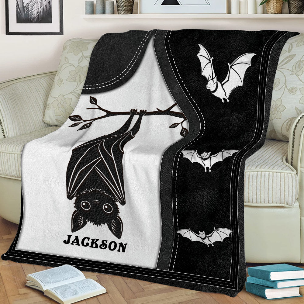 Black and white bat blanket styled across a sofa, featuring a large upside-down bat and flying bats