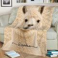 Close-up cream llama blanket styled across a sofa with books and soft neutral decor