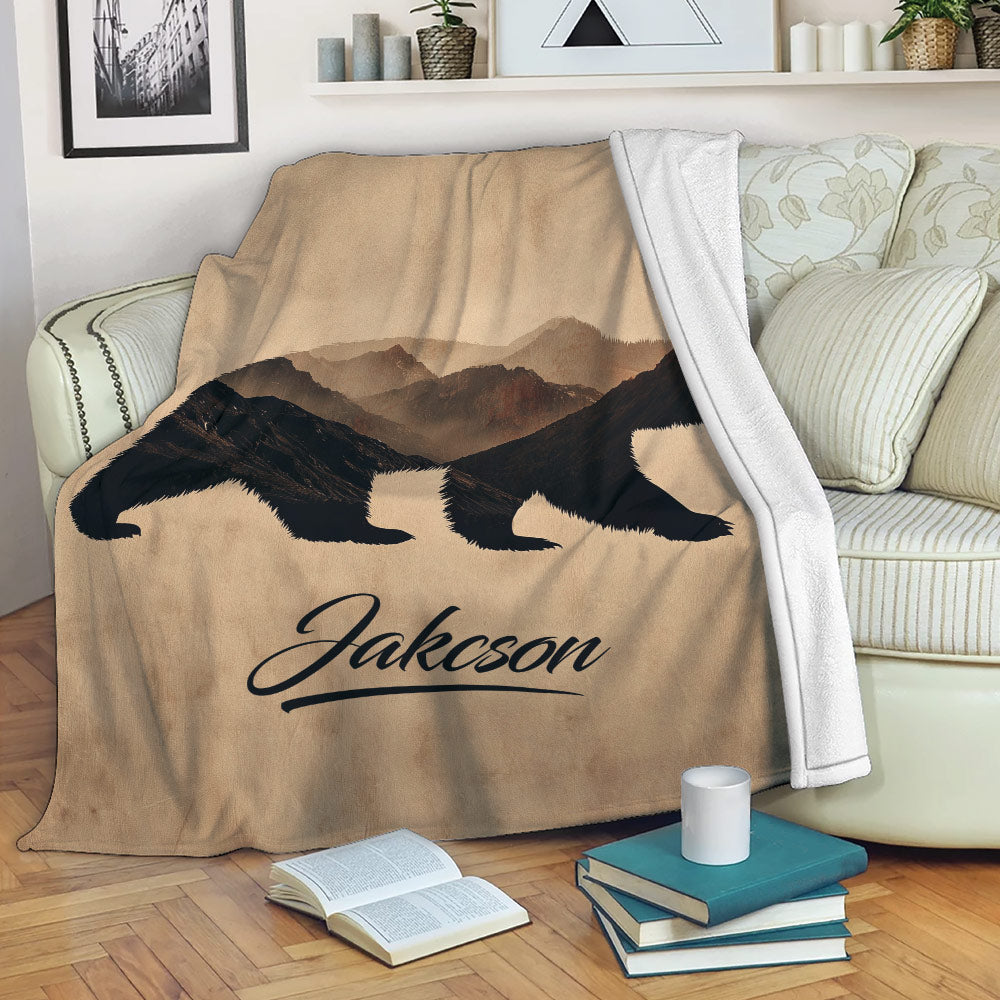 Bear throw blanket draped over a sofa, featuring dark bear silhouettes and a layered mountain landscape