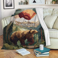 Bear blanket draped over a sofa, showing a mountain forest scene in earthy red, green, and gold tones