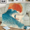 Surfing throw blanket displayed on a couch with a wave-riding surfer and blue, orange, and cream artwork