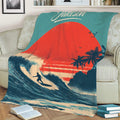 Coastal surfing blanket draped over a couch with a large wave, sunset, palms, and surfer artwork