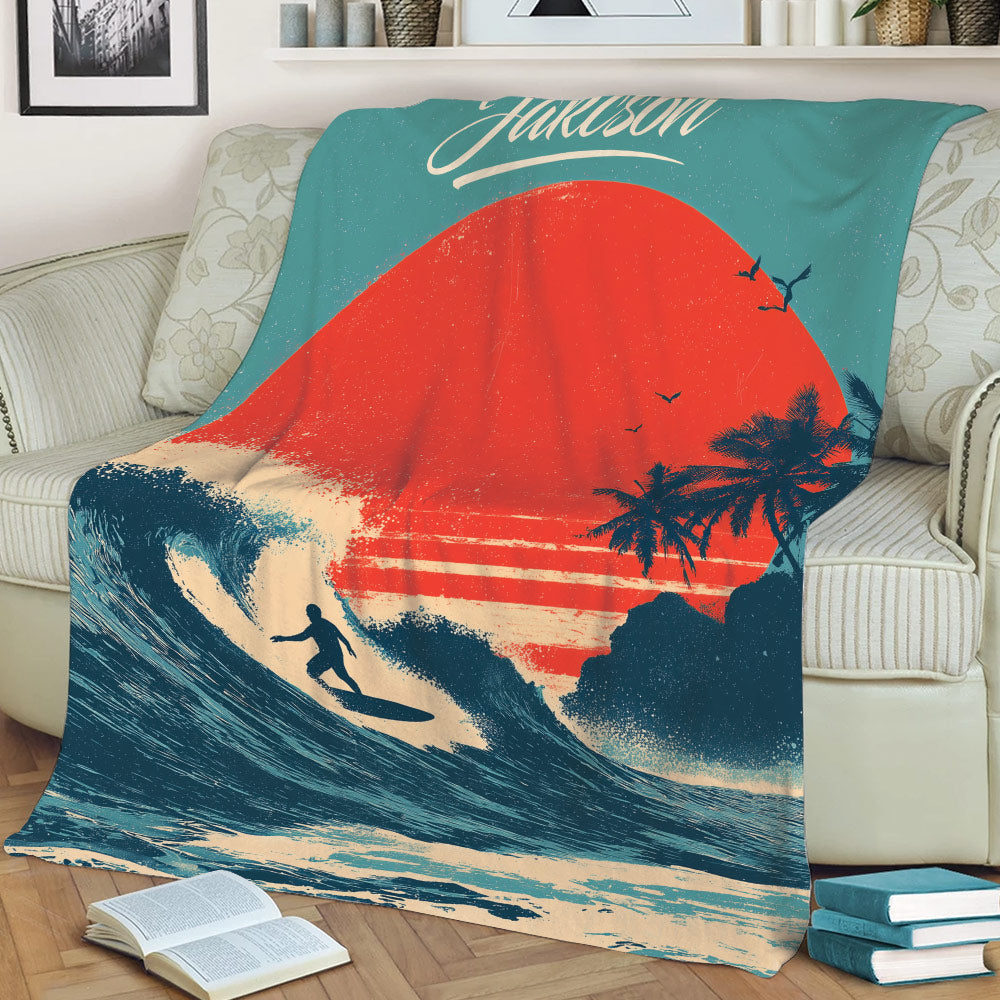 Coastal surfing blanket draped over a couch with a large wave, sunset, palms, and surfer artwork