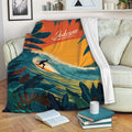 Tropical surfing blanket draped over a sofa, showing a surfer, ocean wave, sunset, and leafy coastal artwork