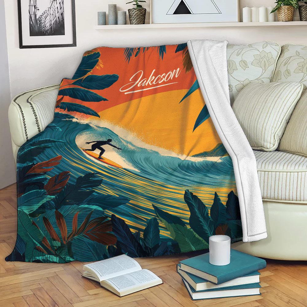 Tropical surfing blanket draped over a sofa, showing a surfer, ocean wave, sunset, and leafy coastal artwork